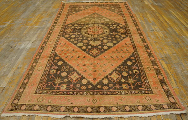 Geometric rug featuring large diamond shapes in peach and brown rests on distressed wood flooring.
