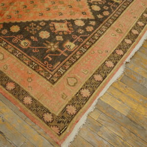 Low-pile rug in coral and dark brown with complex borders resting on distressed plank flooring.
