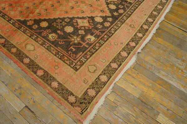 Low-pile rug in coral and dark brown with complex borders resting on distressed plank flooring.