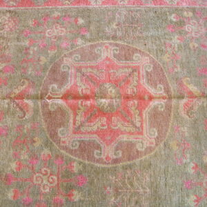 Low-pile rug with a detailed pink medallion and floral pattern on a subdued green background.