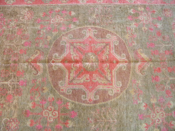 Low-pile rug with a detailed pink medallion and floral pattern on a subdued green background.