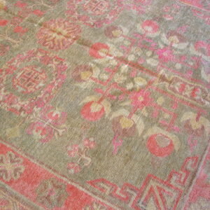 A distressed, low-pile rug features a muted green field with floral and geometric patterns in coral and gold.