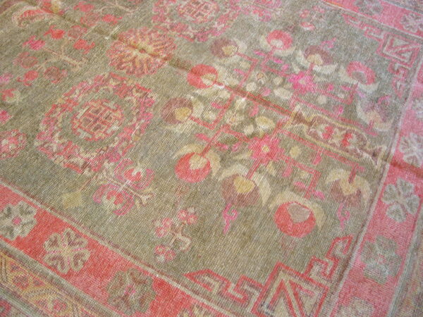A distressed, low-pile rug features a muted green field with floral and geometric patterns in coral and gold.