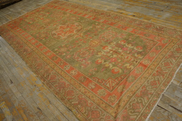 Faded green and coral patterned rug with an ornate medallion lying on highly distressed wood plank flooring.