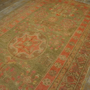 Faded traditional rug in moss green and rust with a medallion design on wide plank wood flooring.