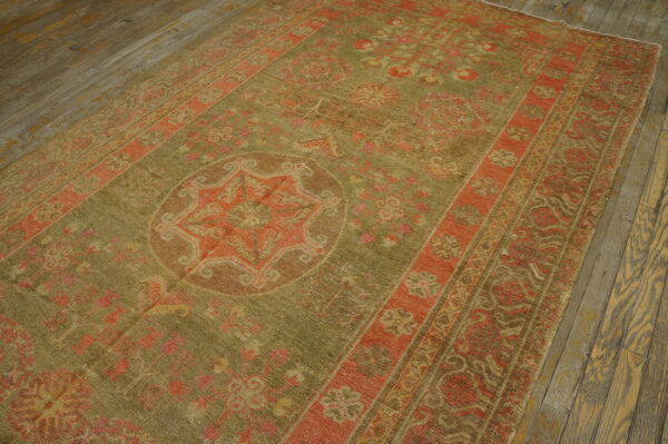 Faded traditional rug in moss green and rust with a medallion design on wide plank wood flooring.