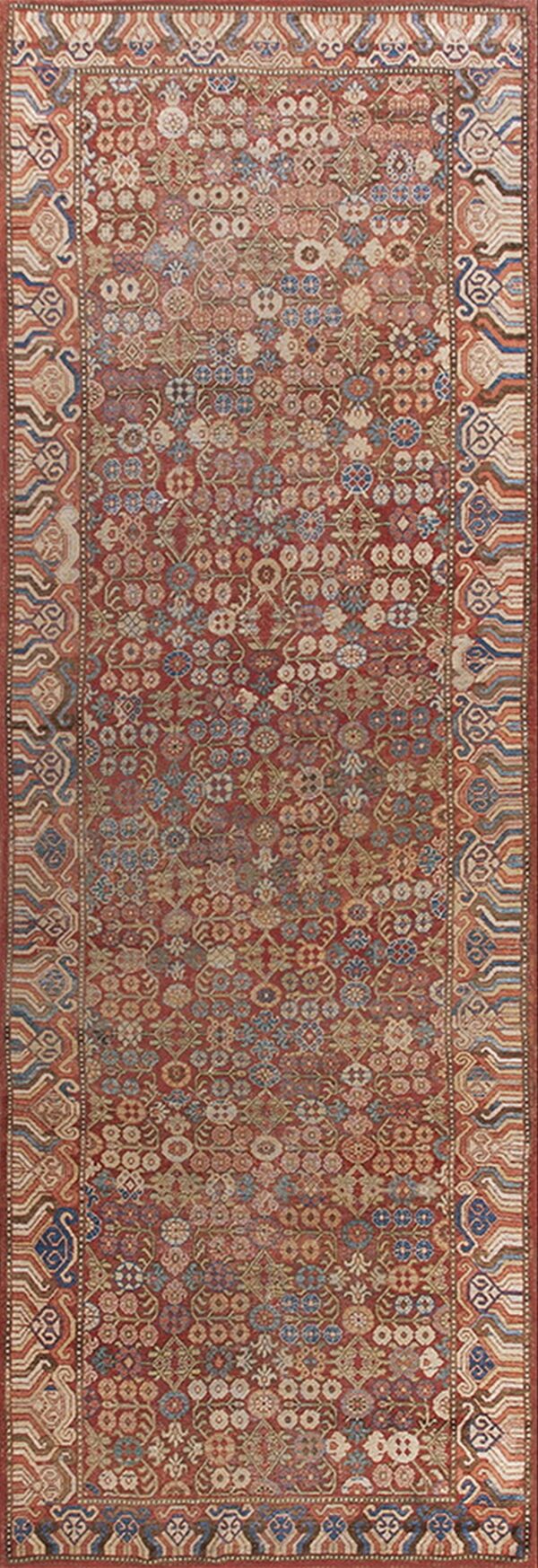 Muted red runner rug features dense stylized motifs and geometric borders in blue, cream, and rust.