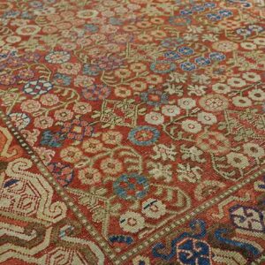 Intricate, low-pile rug with a red field, dense multicolored floral motifs, and geometric borders.