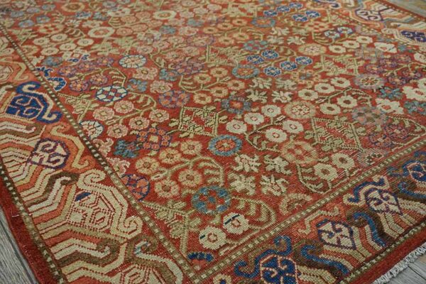 Intricate, low-pile rug with a red field, dense multicolored floral motifs, and geometric borders.