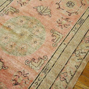 A low-pile rug in faded salmon and beige with a central medallion lies on hardwood flooring.