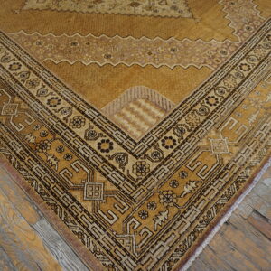 Golden patterned rug corner featuring dark geometric borders rests on distressed gray and brown wood planks.