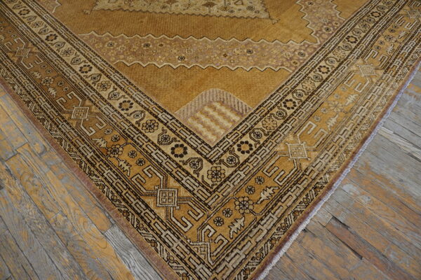 Golden patterned rug corner featuring dark geometric borders rests on distressed gray and brown wood planks.