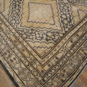 A close-up of a tan and dark brown geometric rug corner lying on medium brown wood flooring.