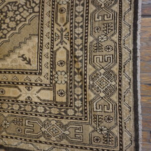 Beige and dark brown traditional rug displaying complex geometric and floral patterns on aged wood floors.