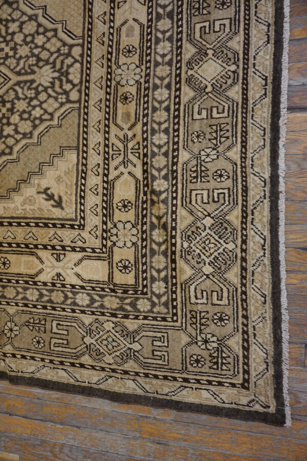 Beige and dark brown traditional rug displaying complex geometric and floral patterns on aged wood floors.