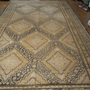 Oversized rug with faded tan diamonds and dark brown floral geometric lattice pattern on wood floor.