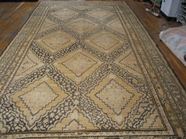 Oversized rug with faded tan diamonds and dark brown floral geometric lattice pattern on wood floor.