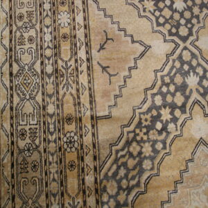 Tan and dark brown rug with a detailed geometric border and stepped medallion pattern on hardwood floors.