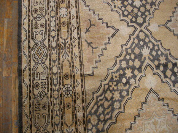 Tan and dark brown rug with a detailed geometric border and stepped medallion pattern on hardwood floors.