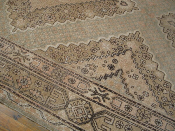 Beige and brown patterned rug detail showing a stepped zigzag border and low pile on wood flooring.