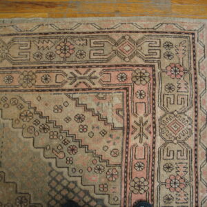 Low-pile rug in earthy tan and pink colors displays geometric borders on light brown wood planks.