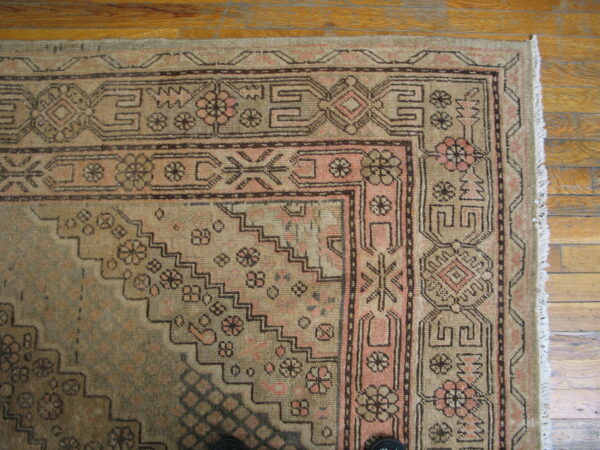 Low-pile rug in earthy tan and pink colors displays geometric borders on light brown wood planks.