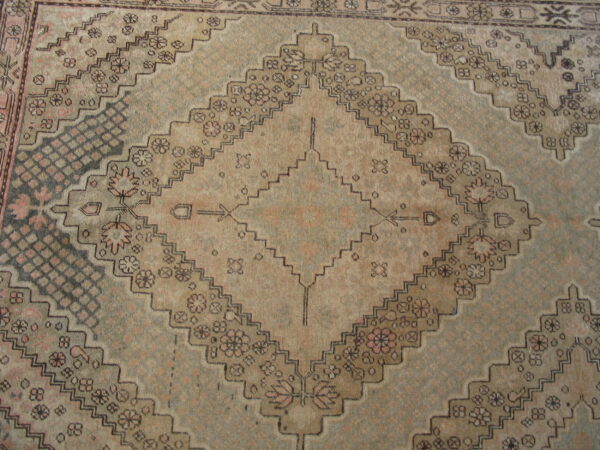 Geometric diamond pattern rug in faded taupe, pale green, and dark brown with small floral motifs.