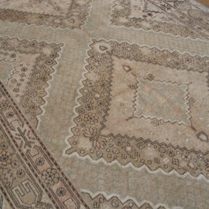 Muted sage and beige low-pile rug with geometric medallions and intricate borders on wood flooring.