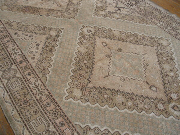 Muted sage and beige low-pile rug with geometric medallions and intricate borders on wood flooring.