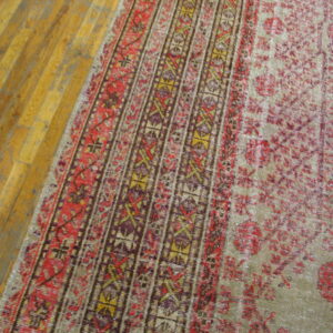 Close-up of a low-pile rug with red, purple, and gold geometric borders on honey-toned wood floors.
