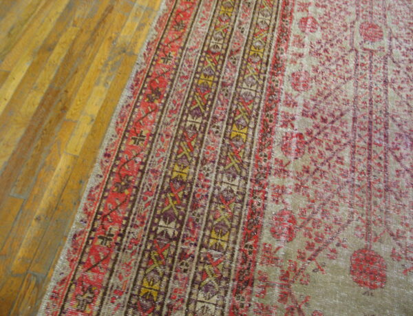 Close-up of a low-pile rug with red, purple, and gold geometric borders on honey-toned wood floors.