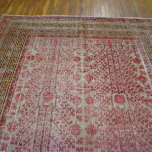 Faded red and beige traditional rug with intricate patterns and a multi-banded border lies on hardwood flooring.
