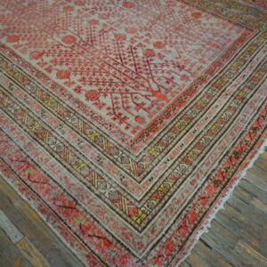 Faded coral and beige rug with geometric borders lies diagonally across distressed wooden plank flooring.