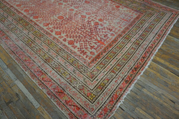Faded coral and beige rug with geometric borders lies diagonally across distressed wooden plank flooring.