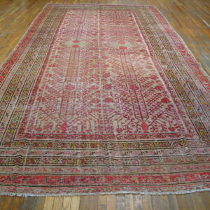 Washed out red and tan low-pile rug with intricate floral motifs and multiple borders over wood flooring.