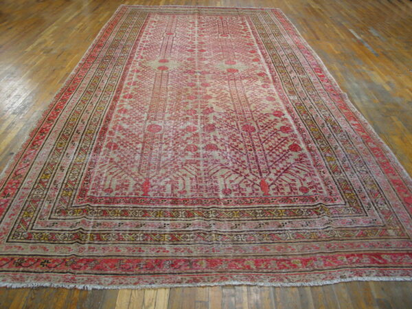 Washed out red and tan low-pile rug with intricate floral motifs and multiple borders over wood flooring.