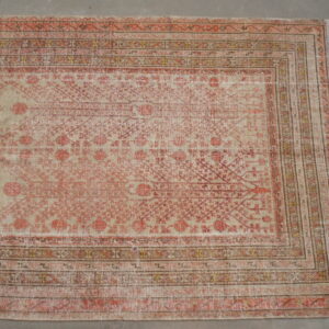 Distressed rug with faded salmon and beige geometric patterns and multi-stripe borders on a gray concrete floor.