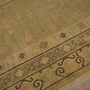 Distressed olive rug featuring faded circular motifs and a dark patterned border on gray wood plank flooring.