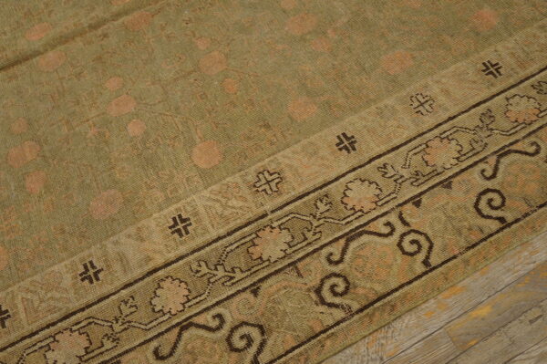 Distressed olive rug featuring faded circular motifs and a dark patterned border on gray wood plank flooring.