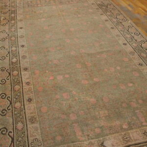 Distressed green and pink rug with geometric borders rests on light brown wooden planks.