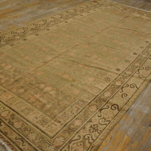 A large olive green rug with pink medallions and a complex border sits on distressed wood flooring.