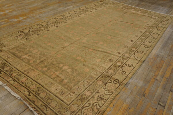 A large olive green rug with pink medallions and a complex border sits on distressed wood flooring.