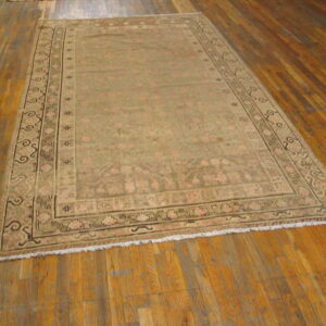 Low-pile traditional rug in muted khaki and faded pink rests on distressed wood plank flooring.