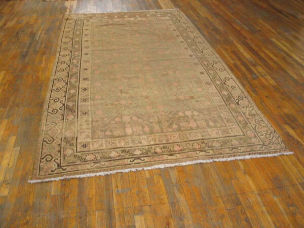 Low-pile traditional rug in muted khaki and faded pink rests on distressed wood plank flooring.