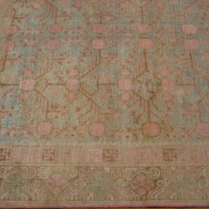 Low-pile rug with geometric pink, tan, and pale blue patterns, including stylized medallions and layered borders.