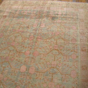 Muted sage and pink low-pile rug with a repeating botanical pattern rests on dark plank wood flooring.