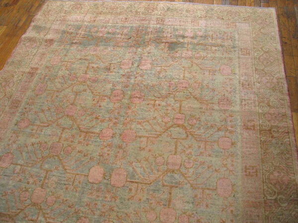 Muted sage and pink low-pile rug with a repeating botanical pattern rests on dark plank wood flooring.