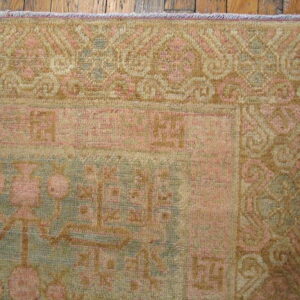 Faded traditional rug corner featuring pink, muted green, and tan patterns resting on wood planks.
