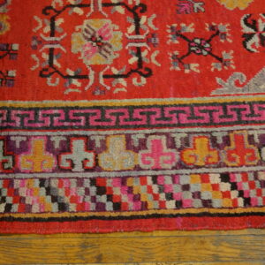 Red textured rug border with pink, purple, yellow, and geometric patterns rests on warm wood floor planks.