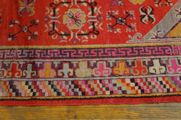 Red textured rug border with pink, purple, yellow, and geometric patterns rests on warm wood floor planks.
